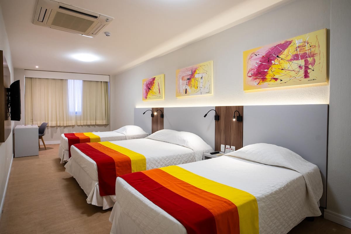 Una habitación de hotel con tres camas, un escritorio y un televisor.