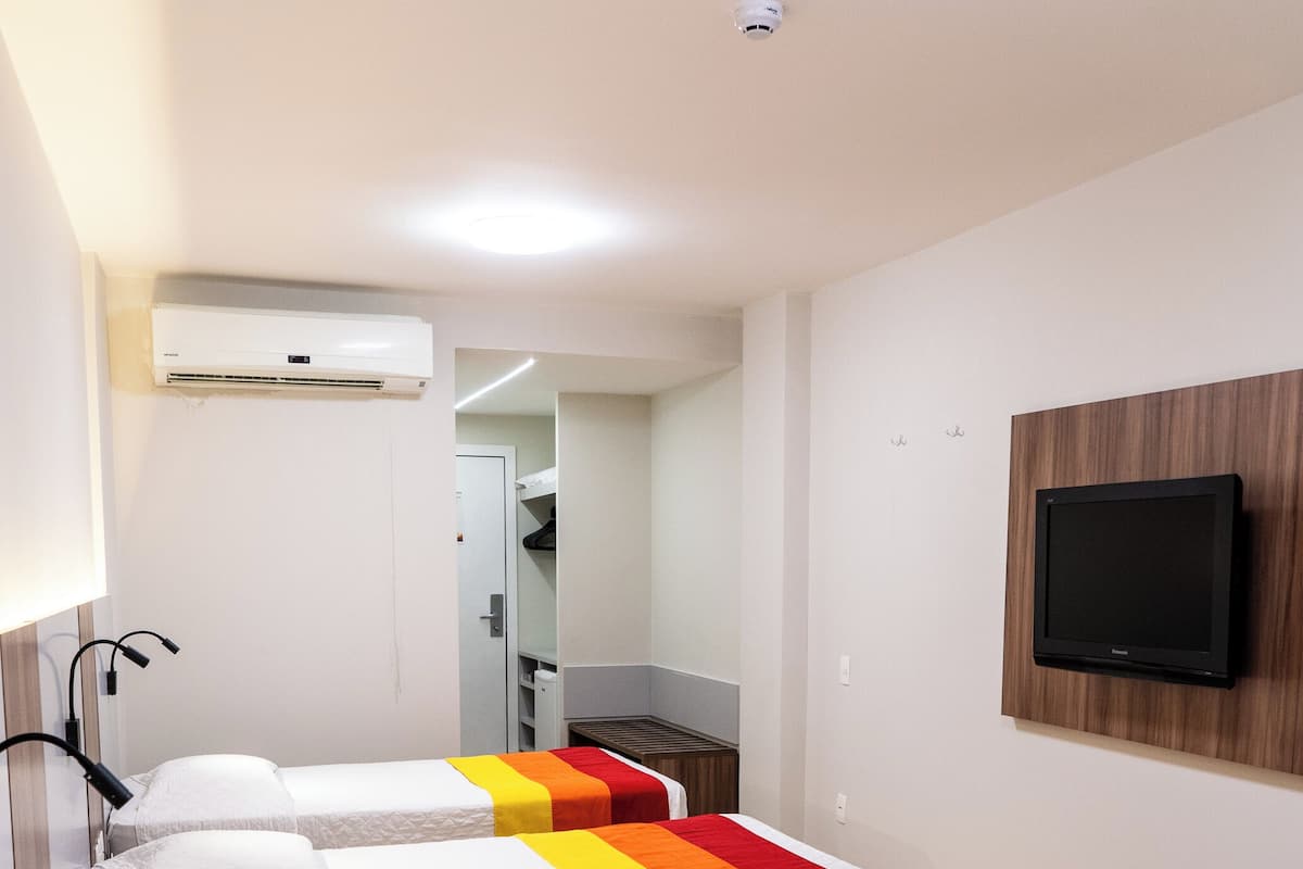 Habitación de hotel con tres camas, un televisor montado en la pared y un equipo de aire acondicionado.
