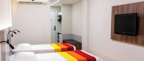 Habitación de hotel con tres camas, un televisor montado en la pared y un equipo de aire acondicionado.