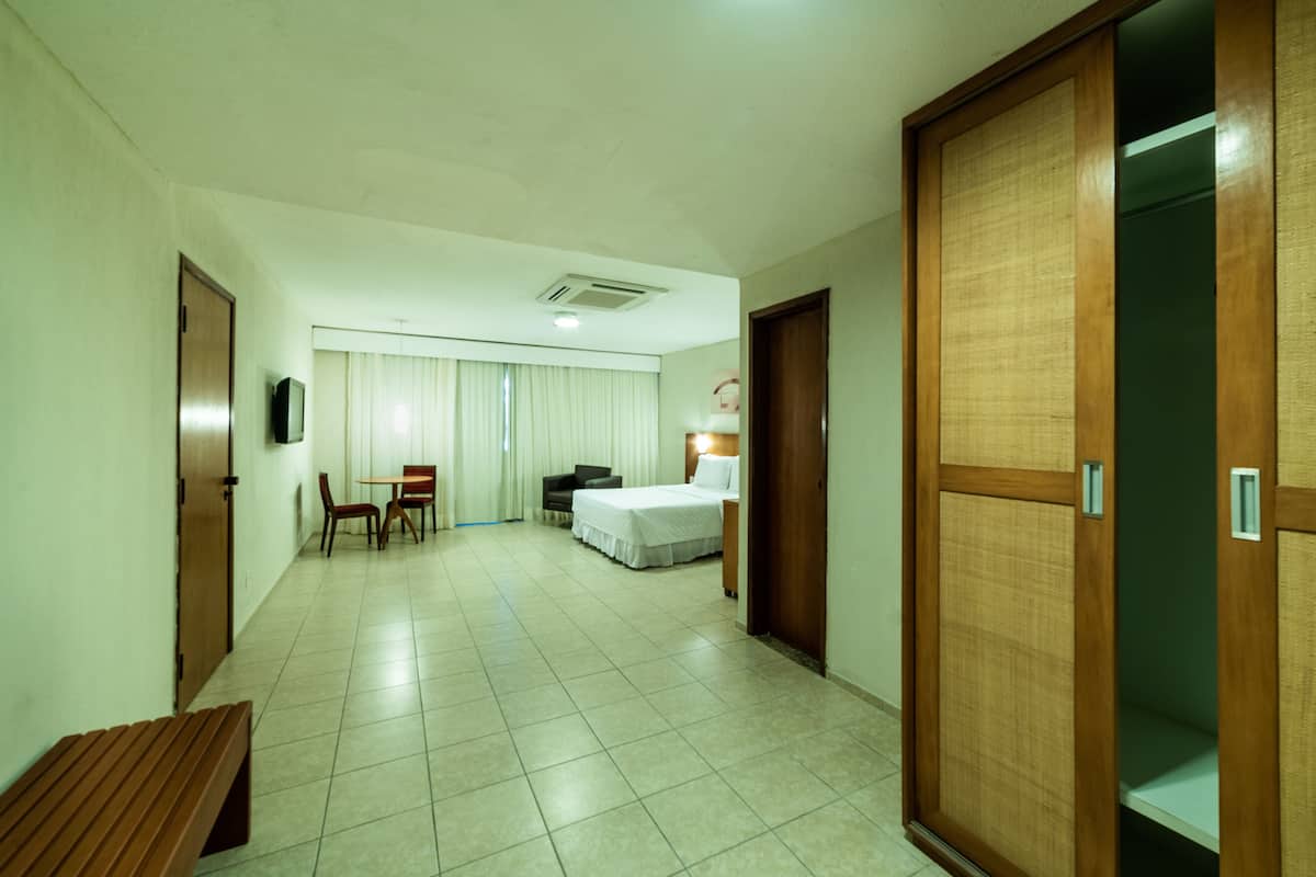 Una habitación de hotel con cama, escritorio, silla, banco y armario.
