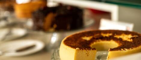 A cheesecake on a glass plate with a slice missing, and a blurred background with other desserts.