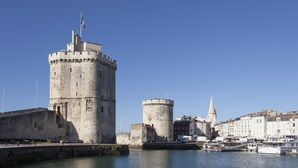 A historic stone castle with a prominent tower, a church spire, and a marina with boats.
