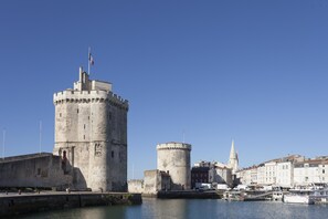 A historic stone castle with a prominent tower, a church spire, and a marina with boats.