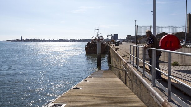A pier with a boat docked, a metal railing, and a clear view of the water.