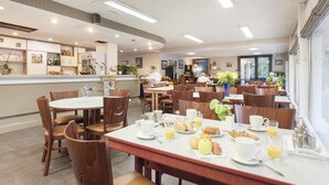 A dining area with tables and chairs, breakfast items, and a counter with various items.