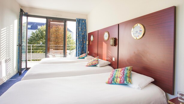 A hotel room with two beds, a wooden headboard, a large window with a view of the outdoors, and a balcony.
