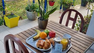Una mesa con una bandeja de alimentos para el desayuno, incluyendo croissants, frutas y jugo, ubicada en un balcón con plantas en macetas y vista a la calle.