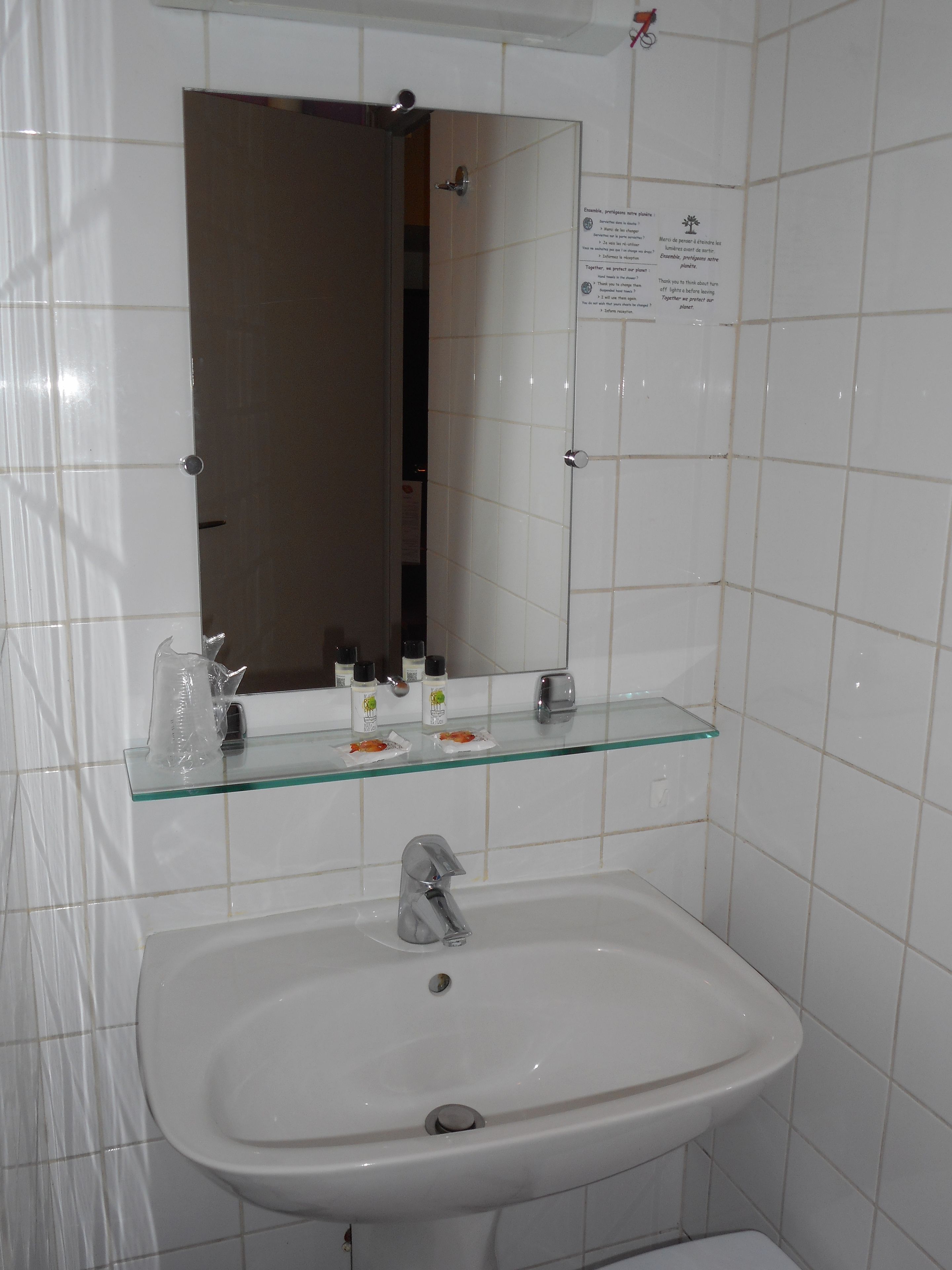 A bathroom with a white sink, a glass shelf with toiletries, and a mirror above the sink.