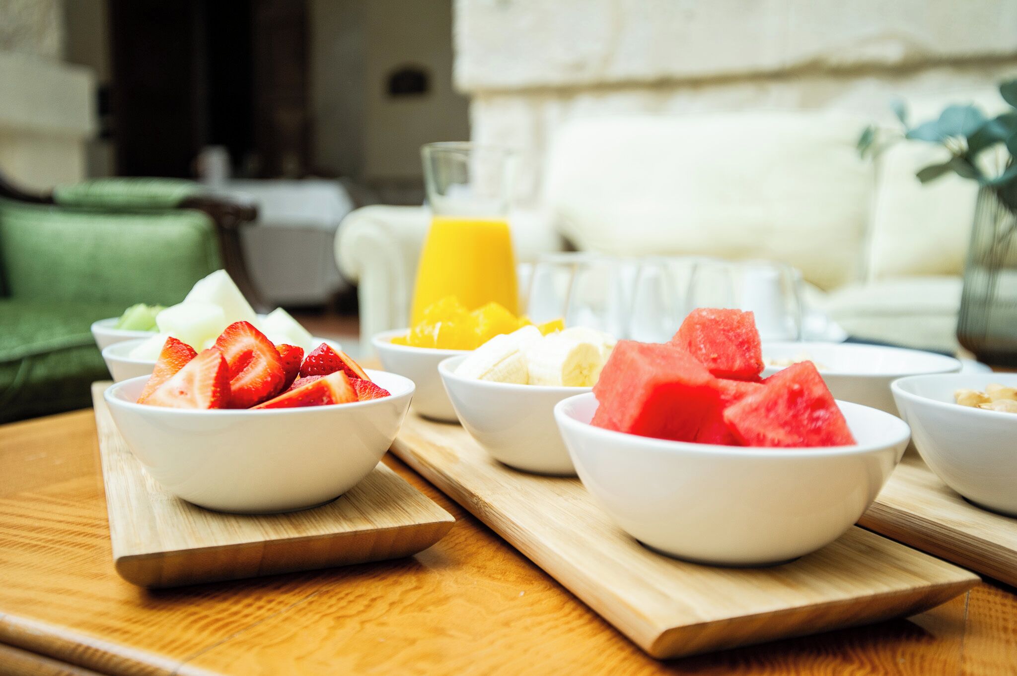 Une table de petit-déjeuner avec des bols de fruits et un verre de jus d’orange, le tout disposé sur une planche en bois.