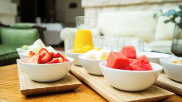 Une table de petit-déjeuner avec des bols de fruits et un verre de jus d’orange, le tout disposé sur une planche en bois.