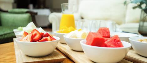 A breakfast setup with bowls of fruit and a glass of orange juice on a wooden board.
