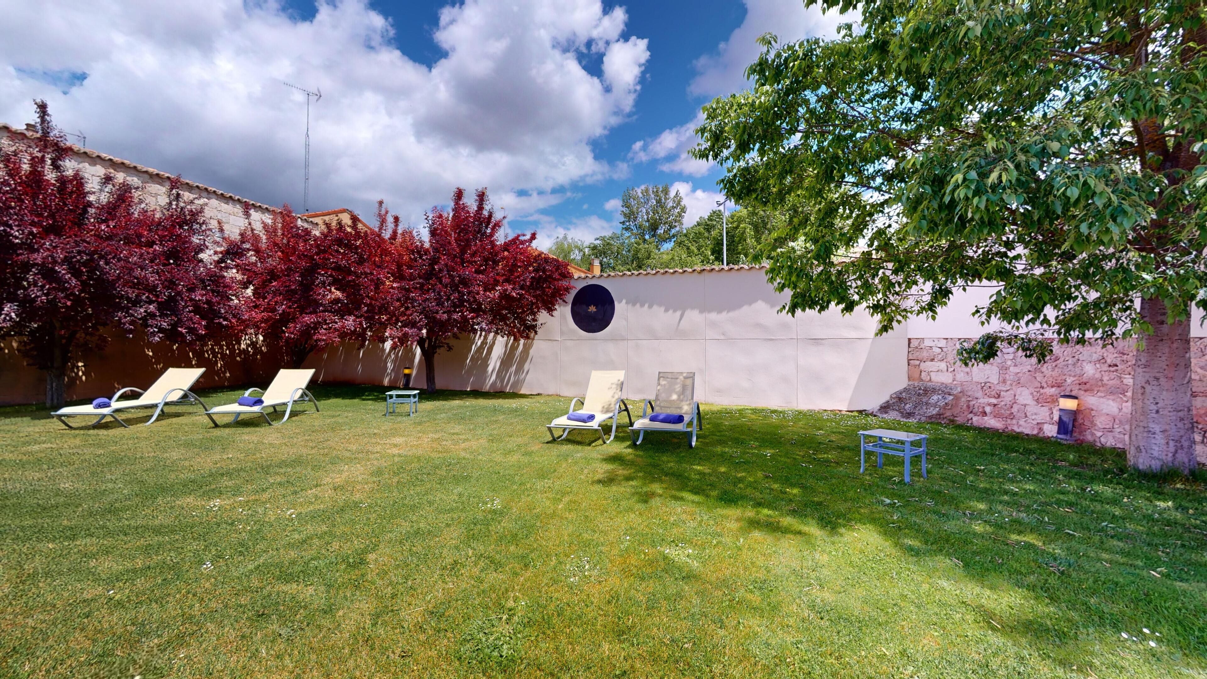 A backyard with a lawn, a wall with a circular window, and several lounge chairs.