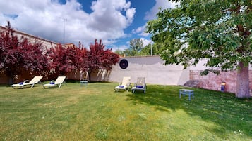 A backyard with a lawn, a wall with a circular window, and several lounge chairs.
