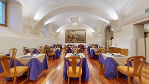 A banquet hall with tables set for dining, wooden chairs, and a large mural on the wall.