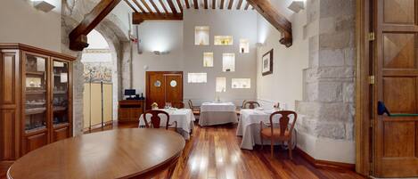 Un comedor con mesas y sillas de madera, paredes de piedra y techo abovedado.