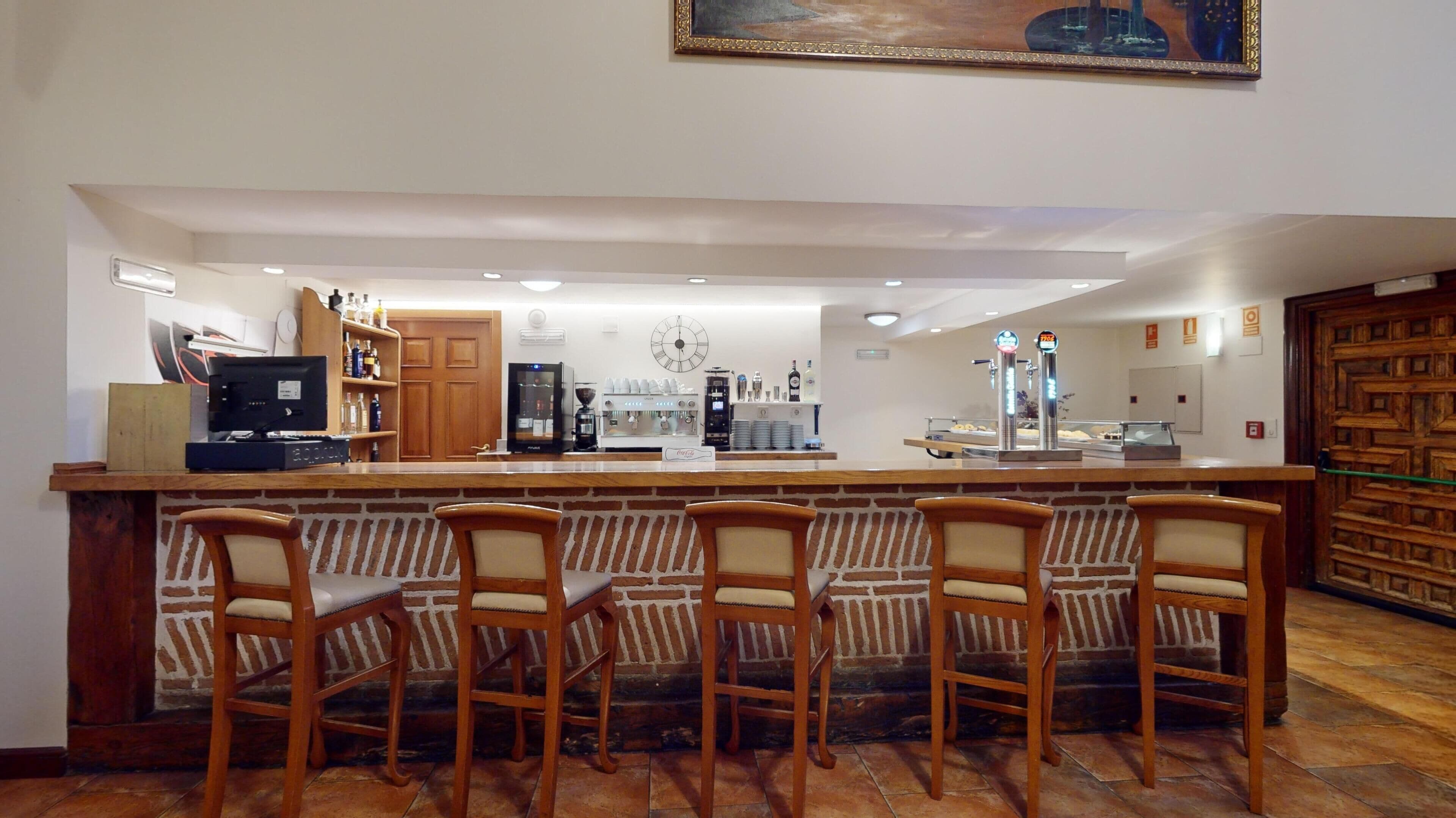 Zona de bar con pared de ladrillo, mostrador de madera y cuatro taburetes.