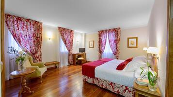 Quarto de hotel com uma cama grande, uma escrivaninha, uma cadeira e uma mesinha com um vaso de flores.