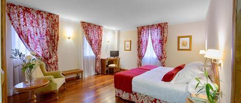 Habitación de hotel con una cama grande, un escritorio, una silla y una mesita con un florero.