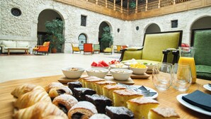 A breakfast setting with pastries, fruits, and juice in a courtyard with stone walls and wooden furniture. - AZZ Peñafiel Las Claras Hotel & Spa (Penafiel)