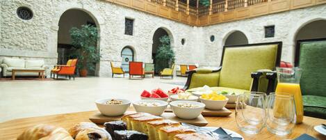 A breakfast setting with pastries, fruits, and juice in a courtyard with stone walls and wooden furniture.