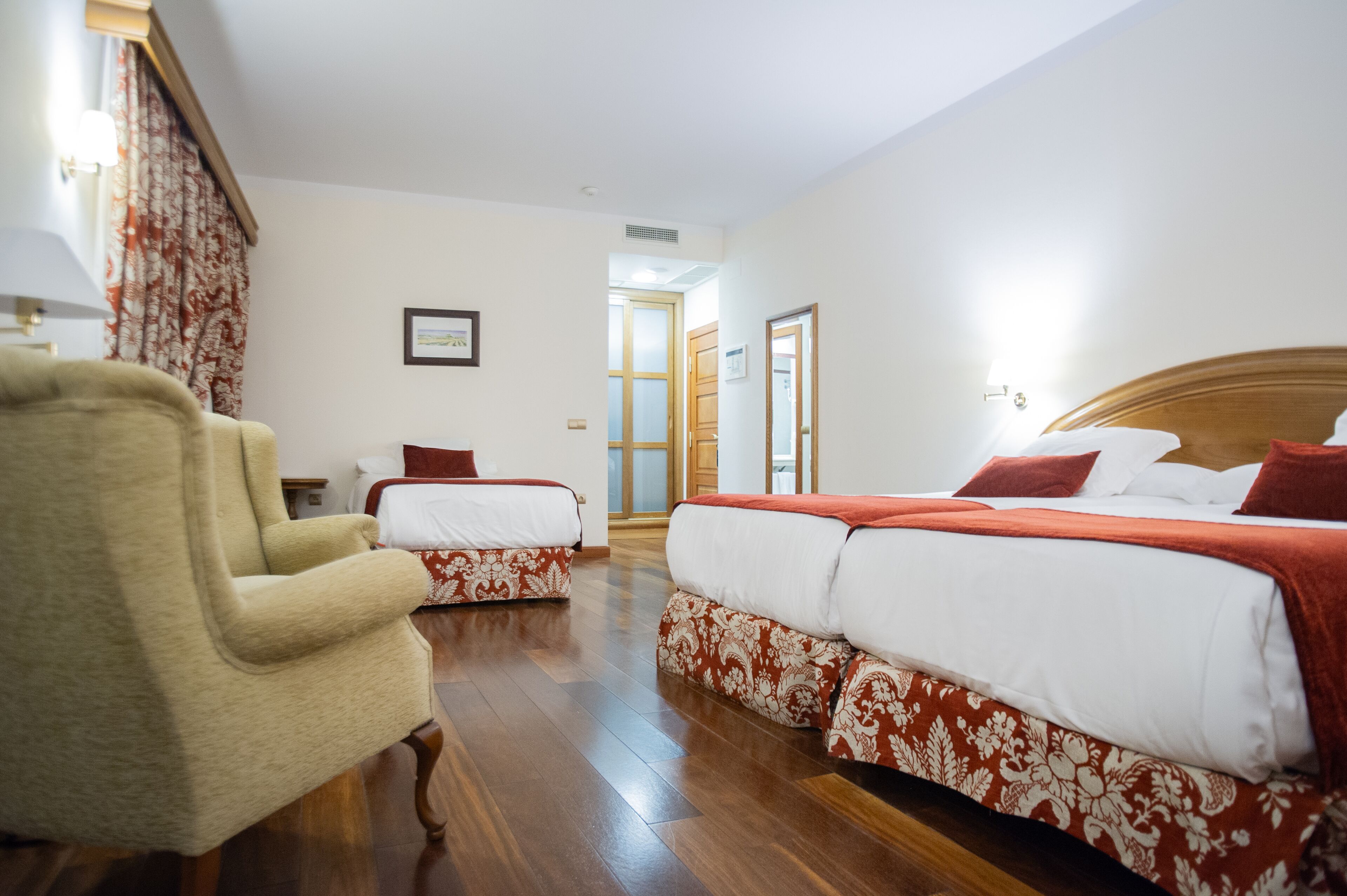 Habitación de hotel con dos camas, piso de madera, una silla y una puerta que da a otra habitación.
