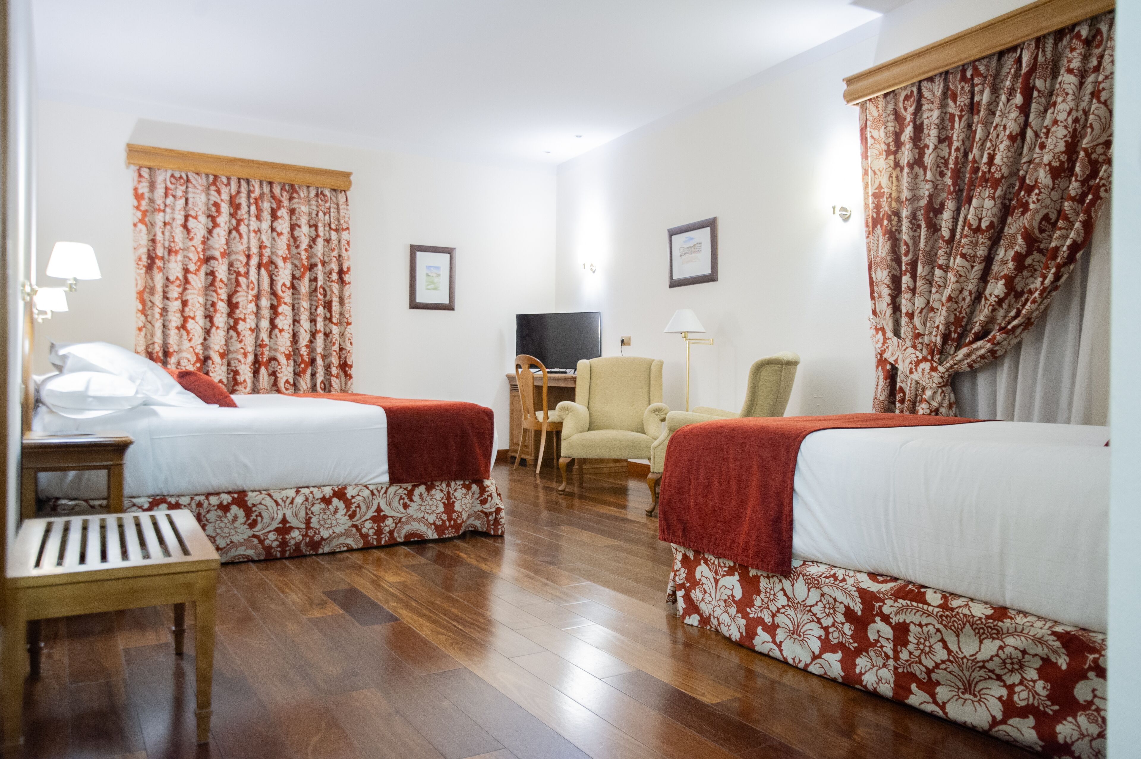Habitació d'hotel amb dos llits, televisió, escriptori i una cadira.
