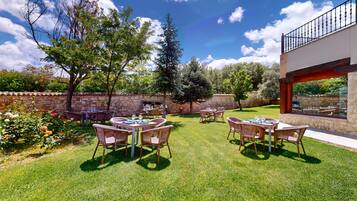 An outdoor patio with tables and chairs, surrounded by stone walls and trees.