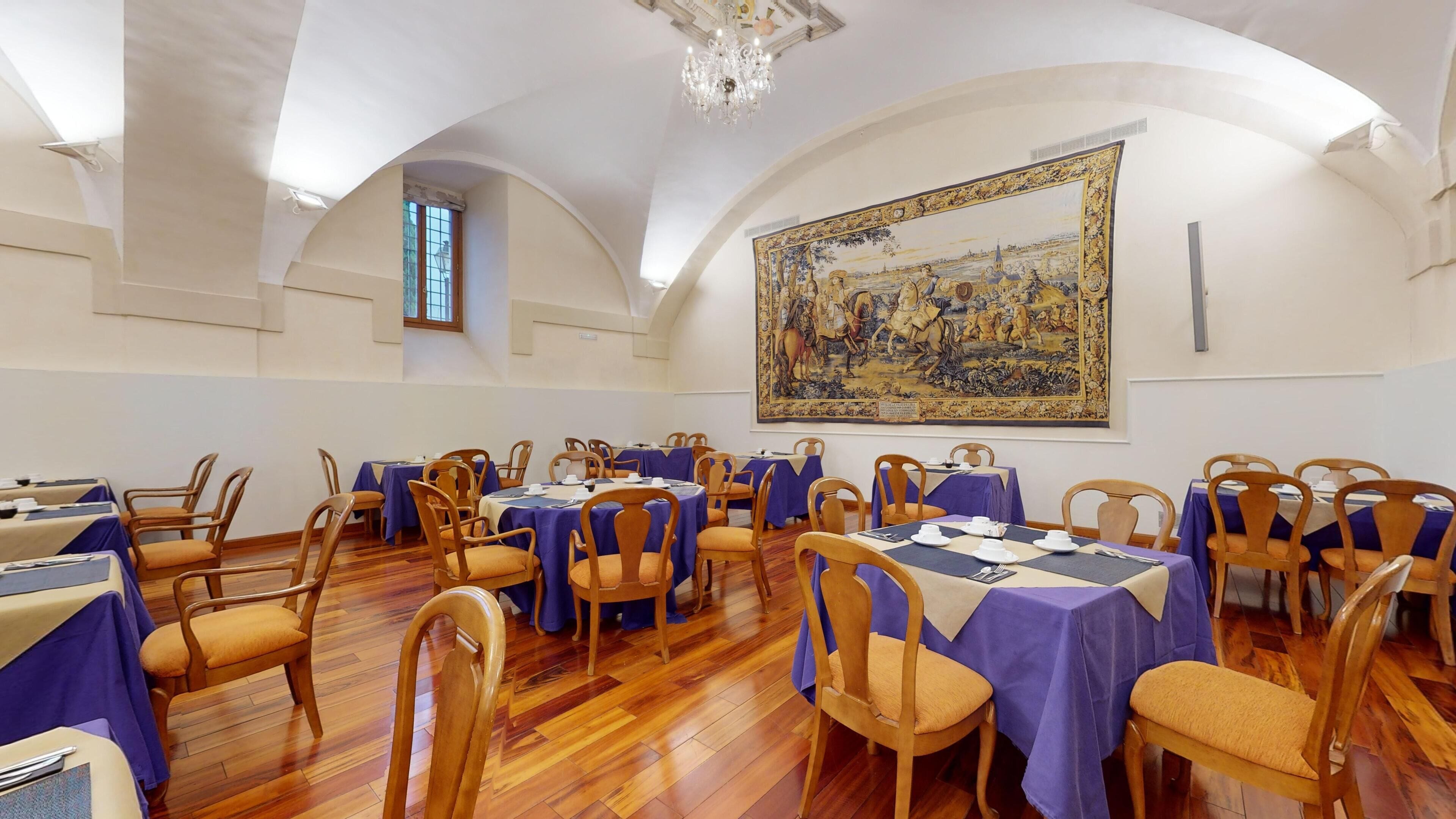 Une salle de conférence avec des tables rondes, des chaises en bois et un grand tableau accroché au mur.