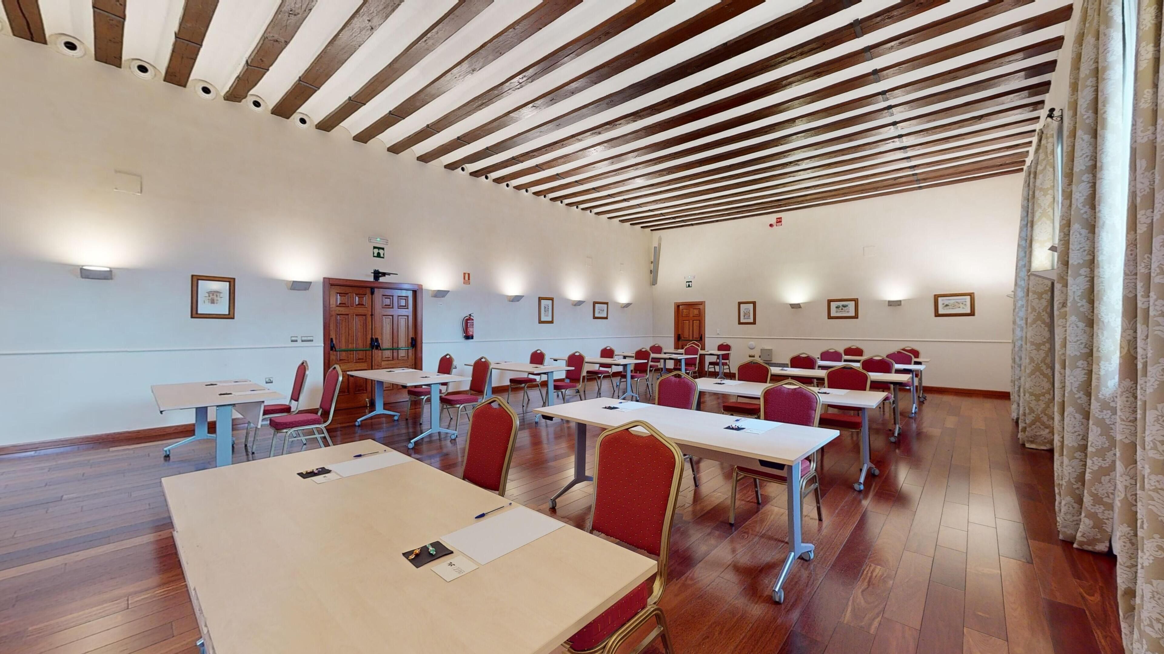 Un salón de conferencias con vigas de madera en el techo, mesas y sillas dispuestas para reuniones.