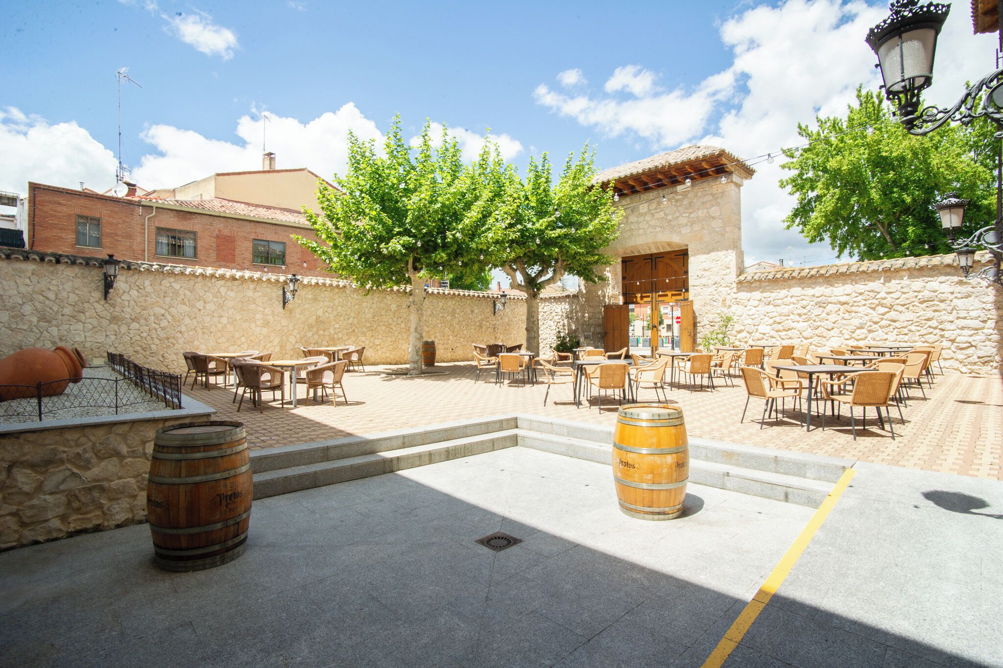 An outdoor patio with stone walls, wooden tables, and chairs, and two wooden barrels.