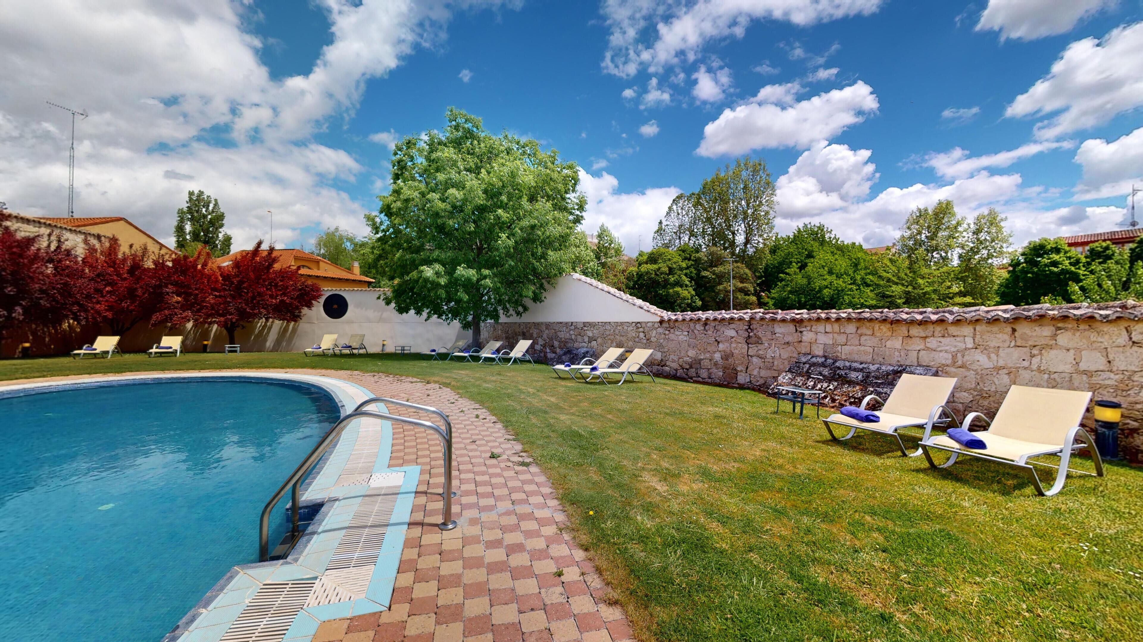A swimming pool with a stone wall and lounge chairs.