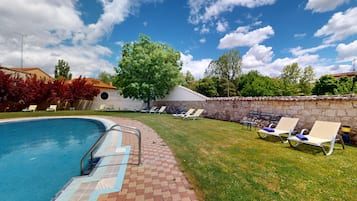A swimming pool with a stone wall and lounge chairs.