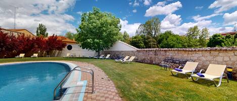 A swimming pool with a stone wall and lounge chairs.