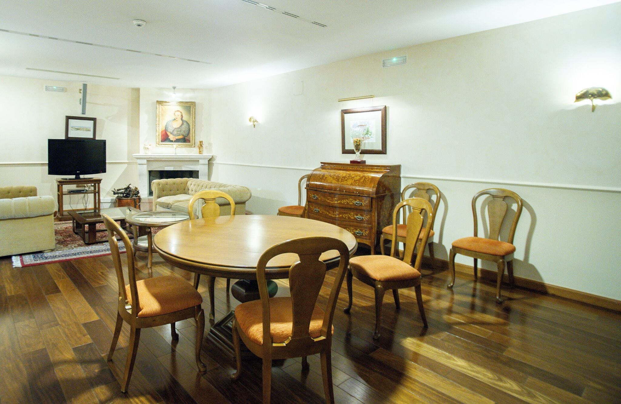 Un comedor con una mesa redonda de madera, seis sillas de madera, un televisor, una chimenea y un cuadro en la pared.