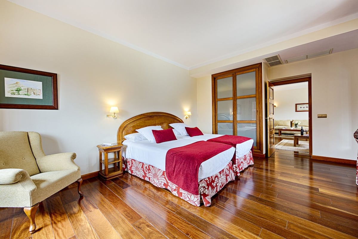 Una habitación de hotel con una cama de madera, una silla, una mesita de noche y un cuadro en la pared.