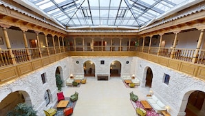 A spacious atrium with a high ceiling and a glass roof, featuring a central seating area with sofas and tables, surrounded by stone walls and wooden railings. - AZZ Peñafiel Las Claras Hotel & Spa (Penafiel)