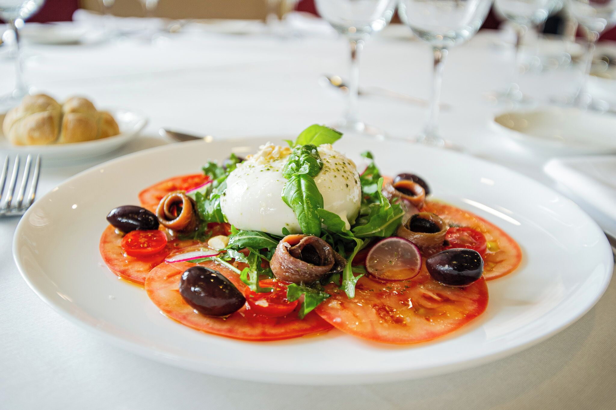 A plate of food with a poached egg, tomatoes, olives, and greens.