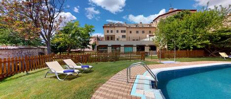 A swimming pool with a wooden deck, lounge chairs, and a stone wall.