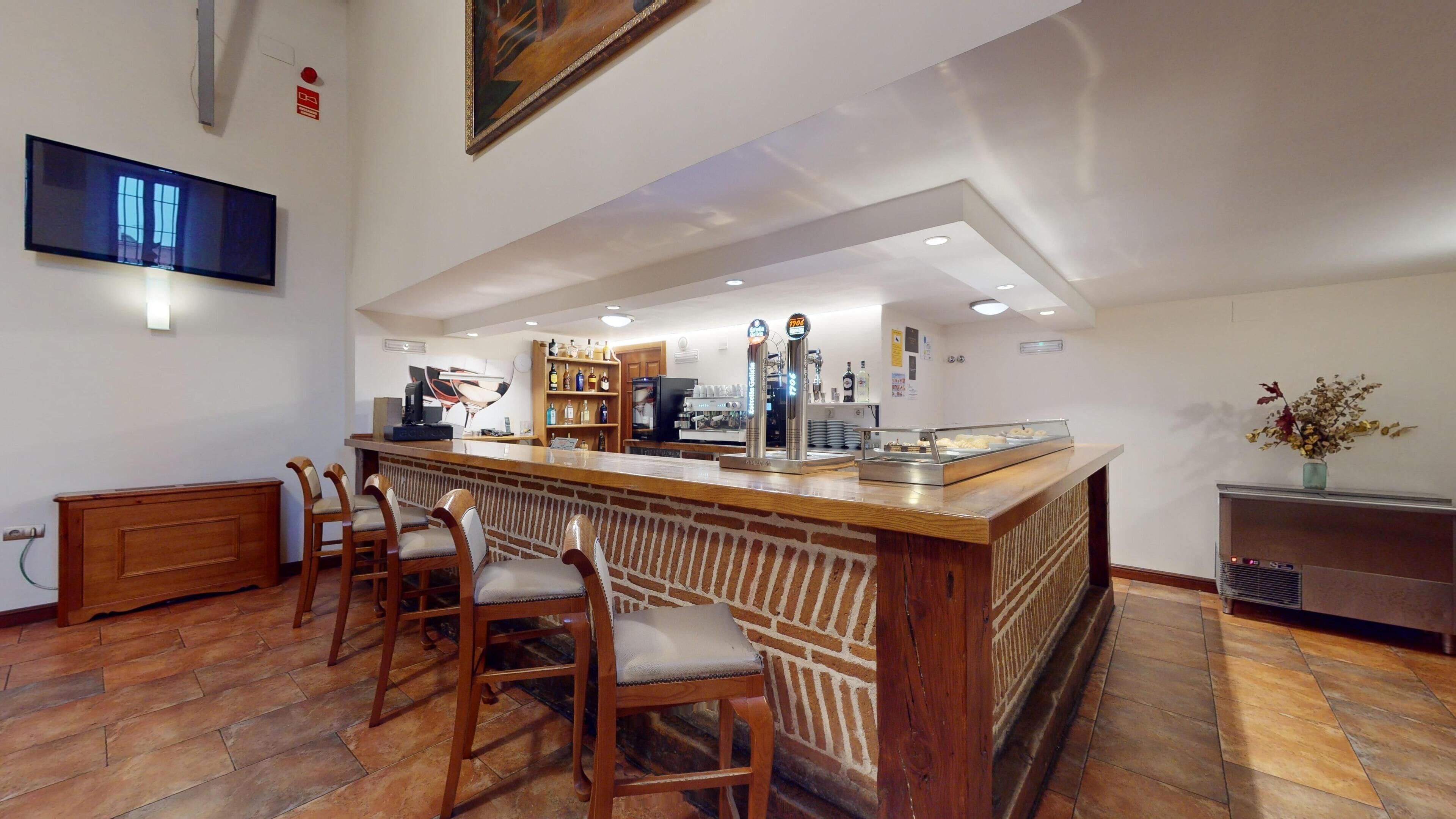 A bar area with a wooden counter, bar stools, a coffee machine, and a display case with pastries.