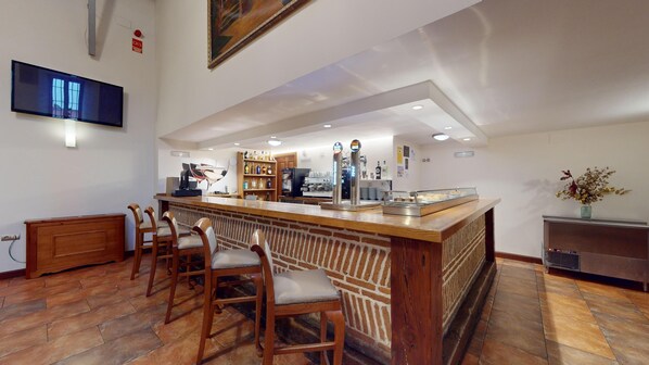Una zona de bar con mostrador de madera, taburetes, una máquina de café y una vitrina con pasteles.