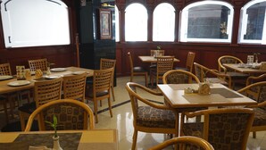 Un restaurante con mesas y sillas de madera, ventanas amplias y un piso limpio de baldosas.