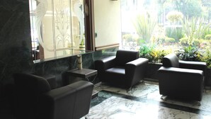 Un vestíbulo con suelo de mármol, sillones de cuero negro, un separador de vidrio con diseños decorativos y vistas a un jardín a través de amplias ventanas.