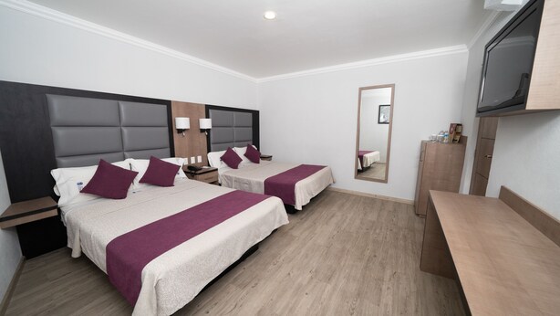 Habitación de hotel con dos camas, un escritorio de madera, un espejo y un televisor.