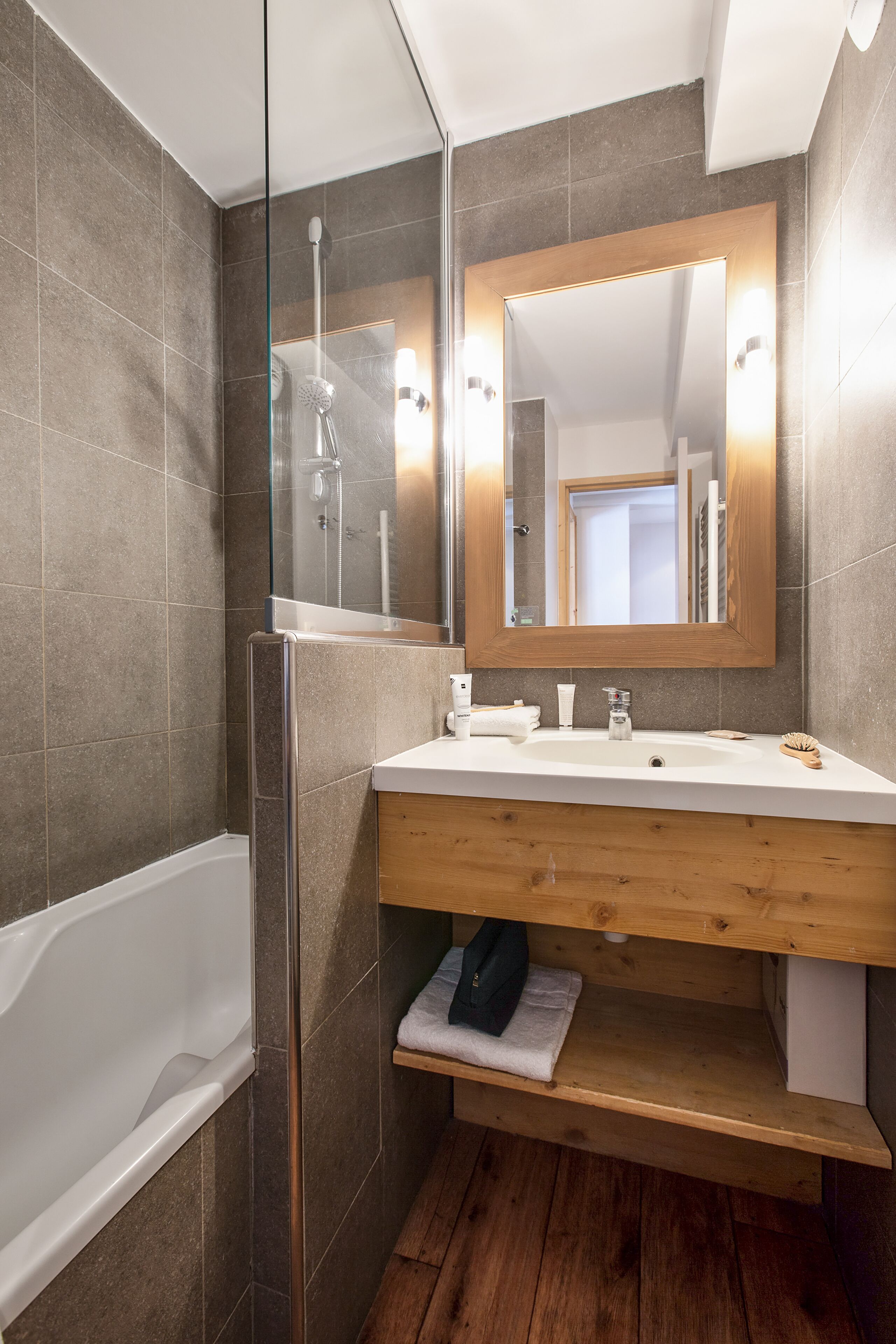 Ein modernes Badezimmer mit einer gläsernen Dusche, einem Holzkosmetikschrank und einem großen Spiegel.