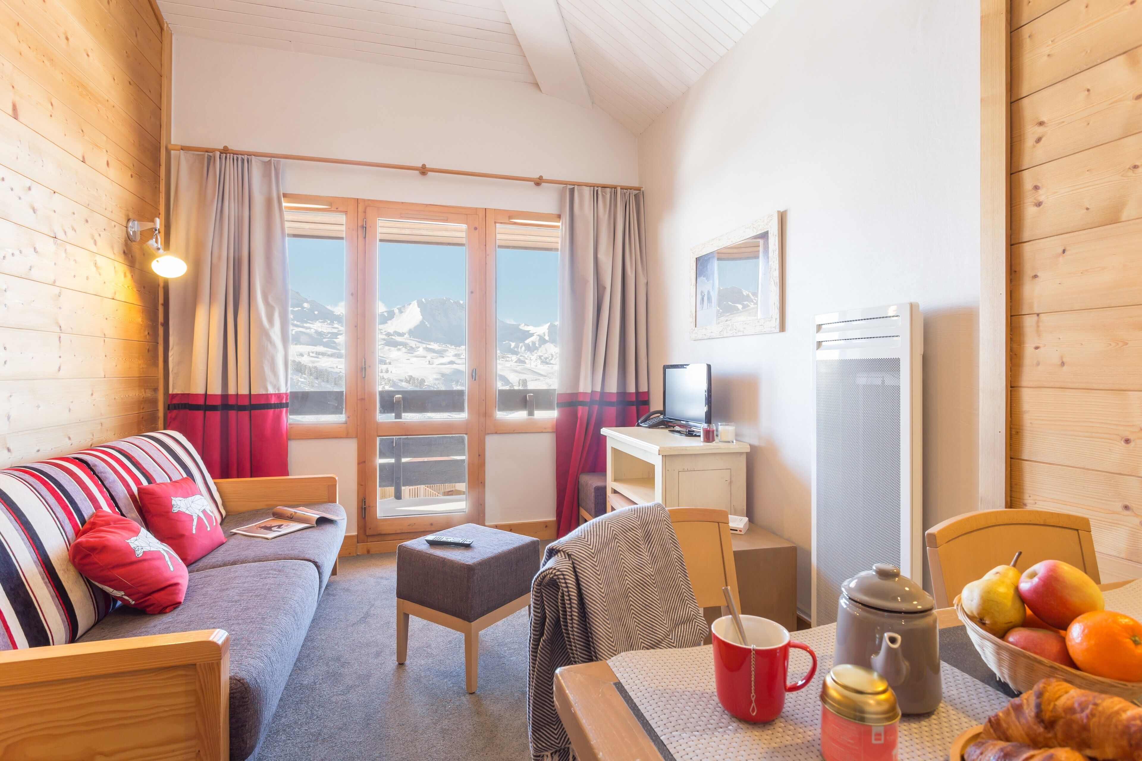 A cozy room with a sofa, a small table with a red mug, a basket of fruit, and a television.