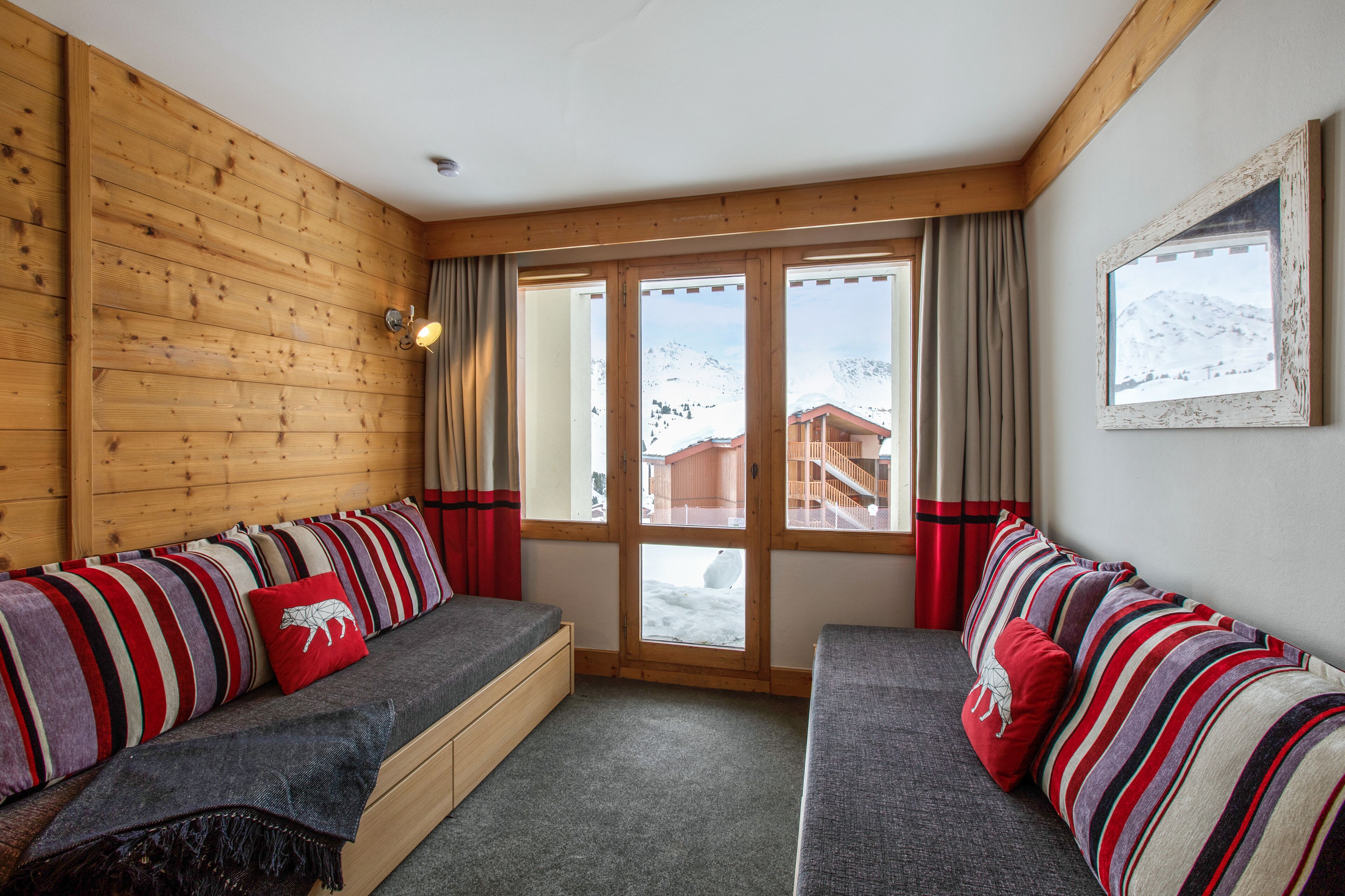 Um quarto acolhedor com parede de madeira, uma janela grande com cortinas e um sofá com almofadas listradas.