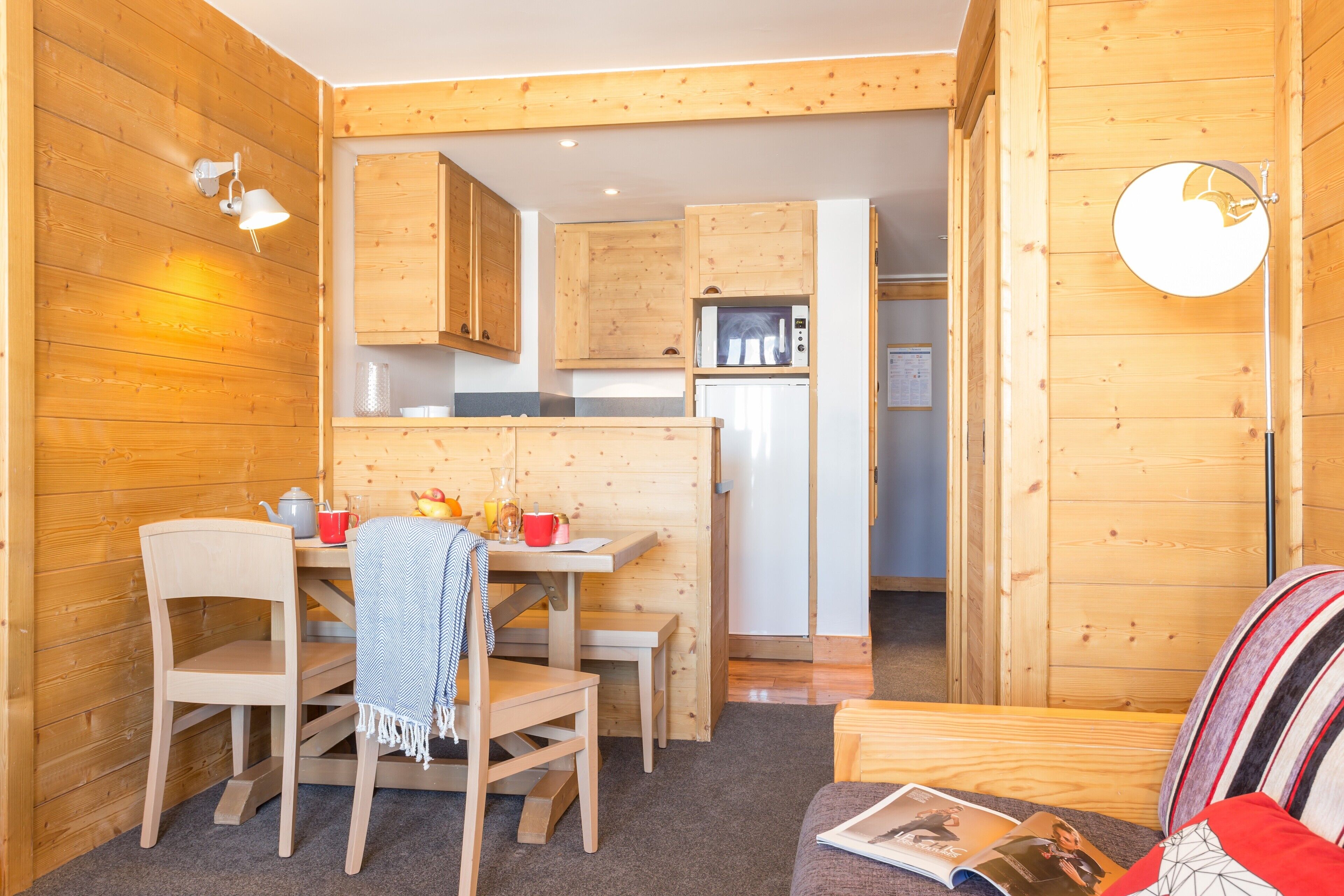 A cozy wooden cabin interior with a dining area, kitchen, and a sofa.