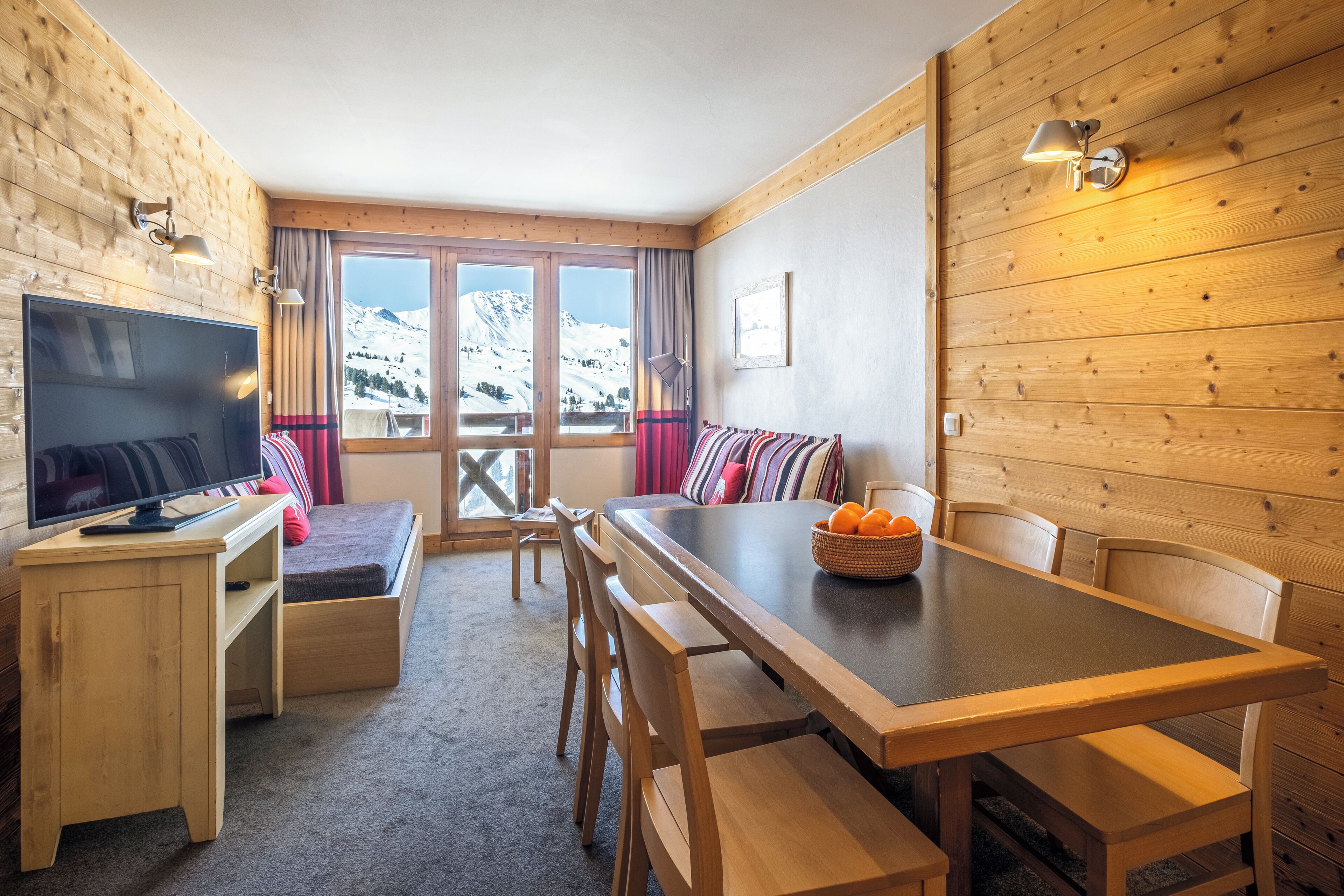 Ein gemütliches Zimmer mit Holzeinrichtung, einem Fernseher, einer Couch und einem Esstisch mit Stühlen.