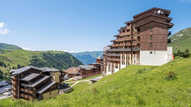 Un hotel de varios pisos con balcones, ubicado en una zona montañosa con cielo despejado.