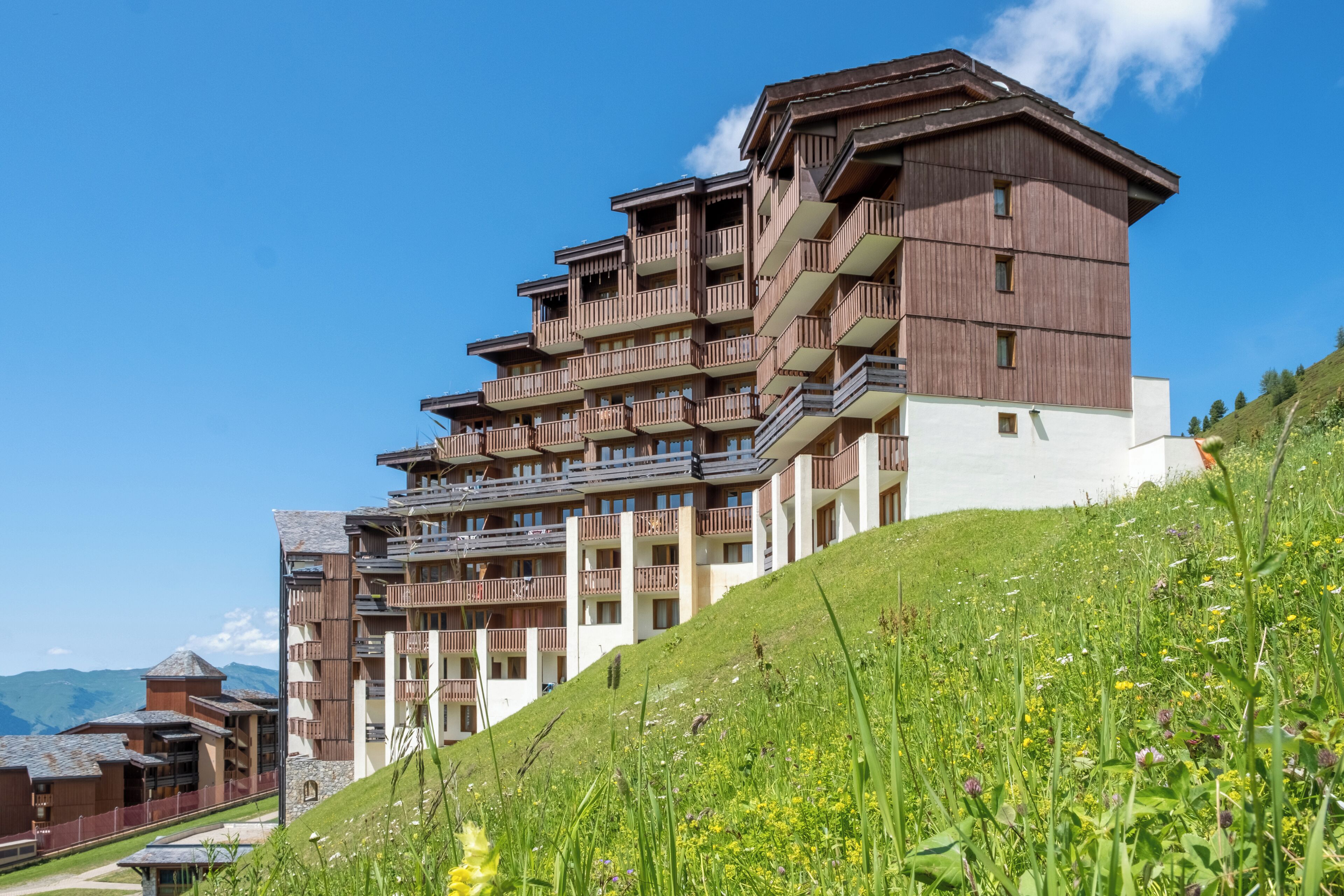 A multi-story hotel with balconies, set on a hillside with a clear sky.